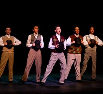 Male cast members of 42nd Street wearing vests and holding hats