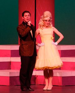 Hairspray host next to a woman in a yellow dress