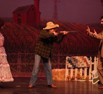 A group of people on a stage with a man holding a gun.