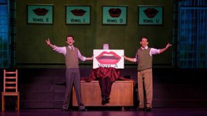 Two men singing while holding a sign for vowels