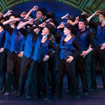 Theater performers wearing black, blue vests, and black hats