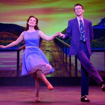 A young man and woman wearing a blue suit and a blue dress dancing together