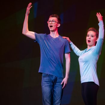 A girl and boy raising their hand while singing
