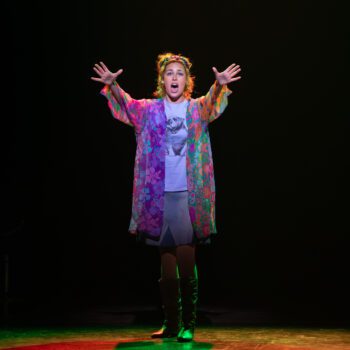 Woman singing on stage in colorful coat.