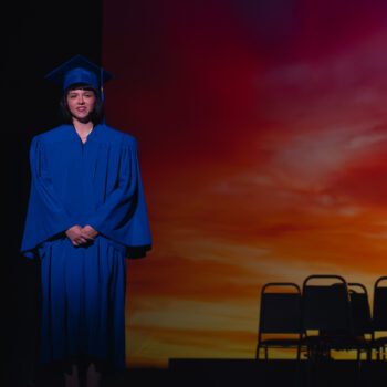Graduate in blue gown on stage.