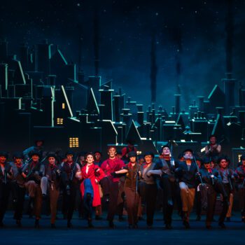 Stage ensemble performing against illuminated city backdrop