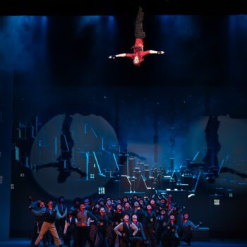 Inverted aerial performer suspended above ensemble