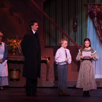 Victorian family gathered on lit theatrical stage