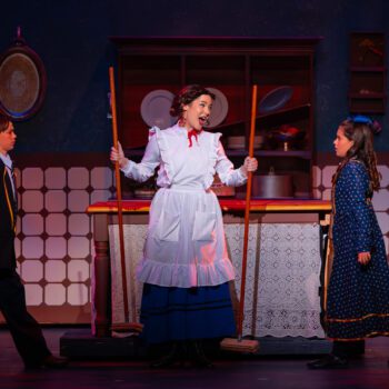 Stage maid holding brooms between two children