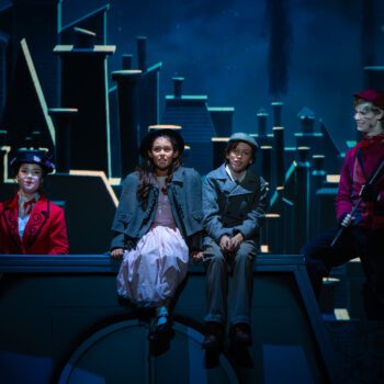 Four performers sitting on rooftop cityscape set