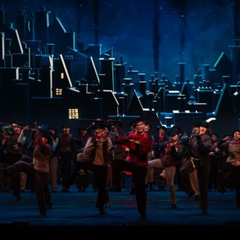 Theatrical ensemble dancing before illuminated city skyline