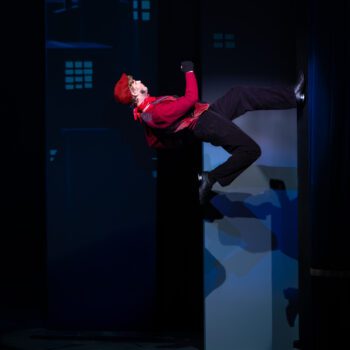 Acrobatic performer in red jacket walking on wall