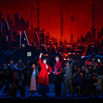 Musical ensemble performing on stage with red skyline