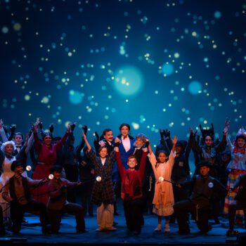 Large musical cast onstage under starry lights