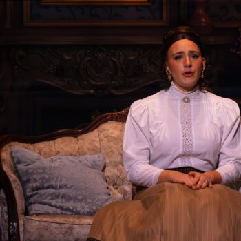 Woman in Victorian costume seated on ornate sofa