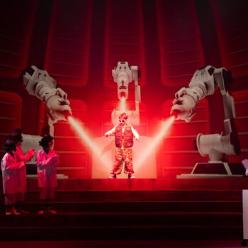 Performer under robotic arms in red spotlight