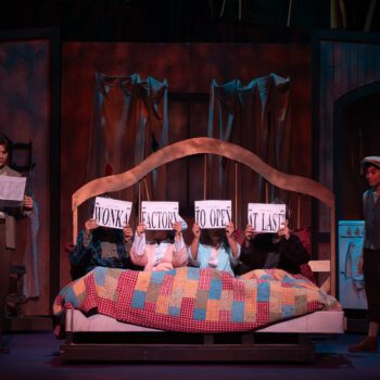 Children on stage in bed with patchwork quilt