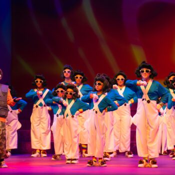 Stage dancers in teal tops and white overalls