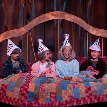 Theatrical actors in bed wearing paper cone hats