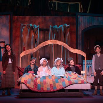 Theatre actors sharing bed under patchwork quilt