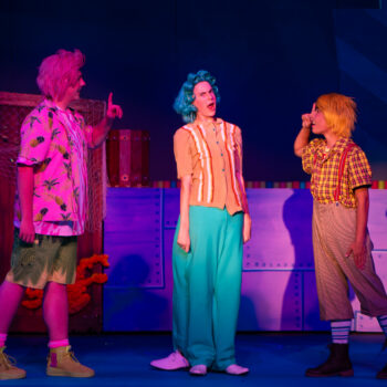 Three costumed actors in colorful theatrical scene