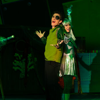 Two performers in green lighting, futuristic costumes
