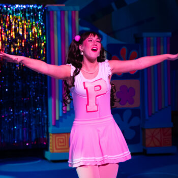 Performer in pink costume singing with arms outstretched