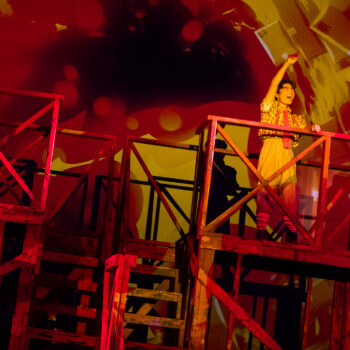 Performer on scaffolding under red and yellow lights