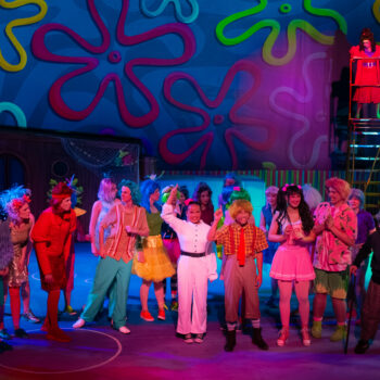 Colorful cast performing on whimsical stage set